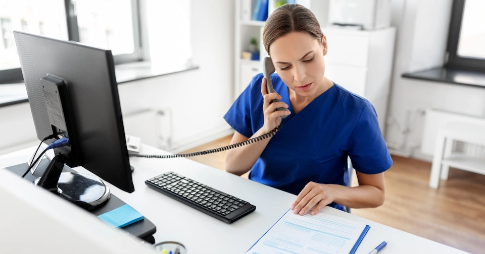Healthcare worker on the telephone while looking at paperwork at a desk in a physician’s office