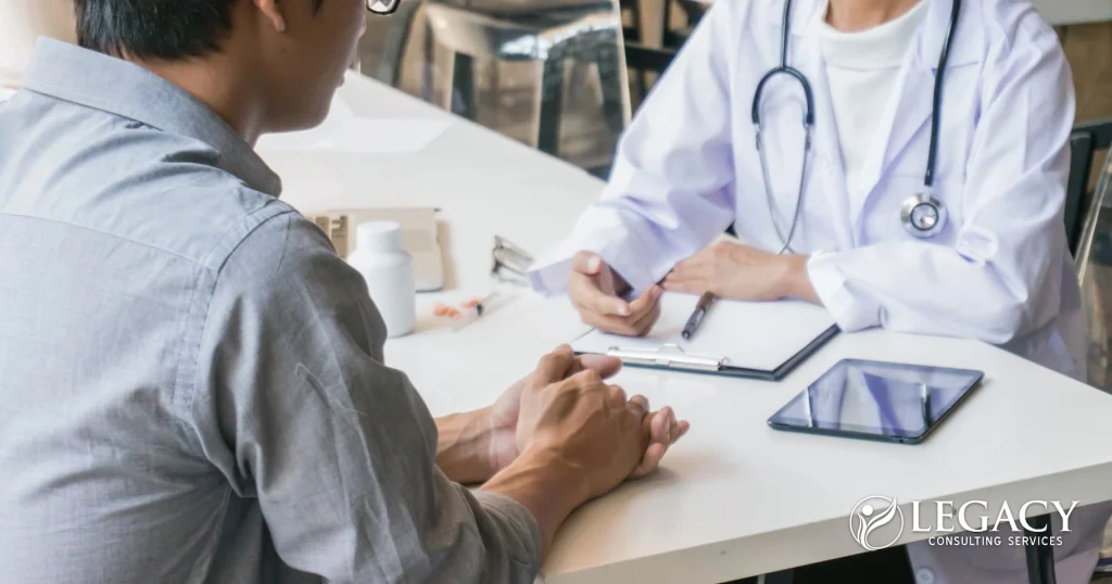 Healthcare provider consulting with a patient during an office visit, discussing care plans across a desk with a clipboard, tablet, and medical supplies, representing patient-centered healthcare and practice operations.